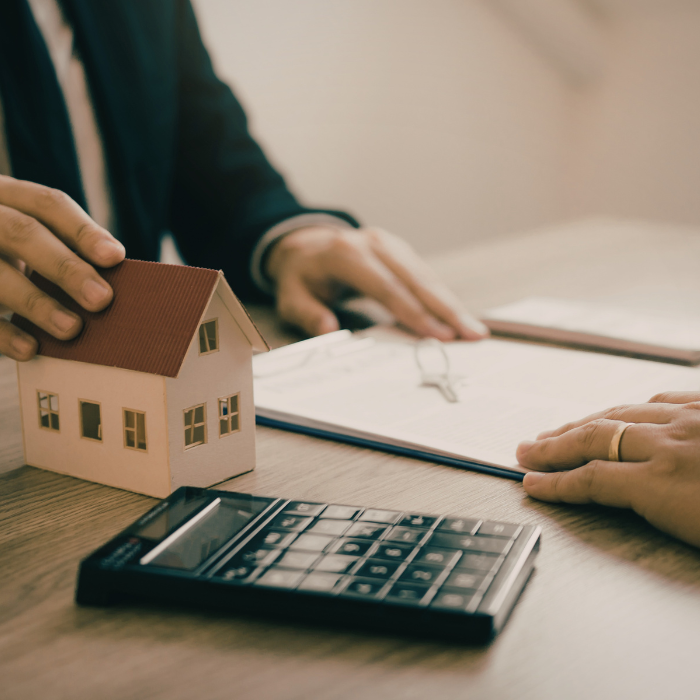 a hand on a house as another hand prepares to sign paperwork