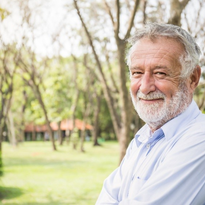 an older man in a white shirt smiles with a house in the background